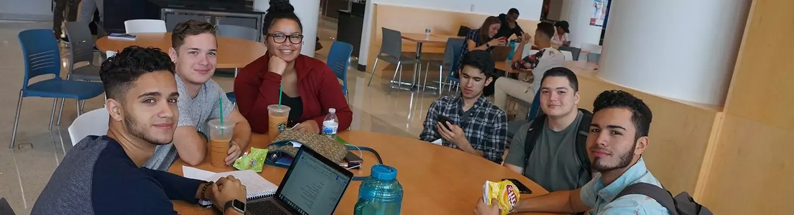 A group of students sitting at a table working and smiling at the camera.