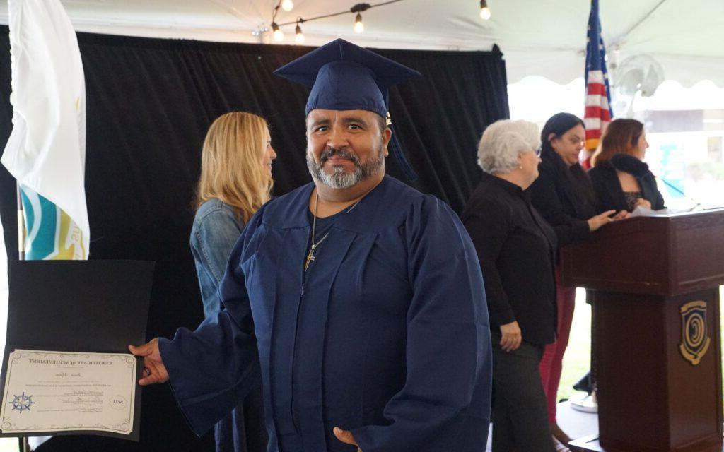 Man with a greying beard in a graduation cap and gown