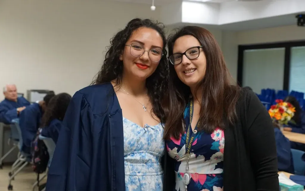 Two females posing in a classroom smiling at the camera